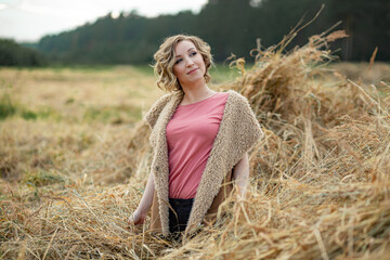 young attractive girl in a fur vest and jeans stands on the hay