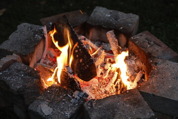 Self made Campfire with embers, ashes, fire wood, stone and coal as close up.