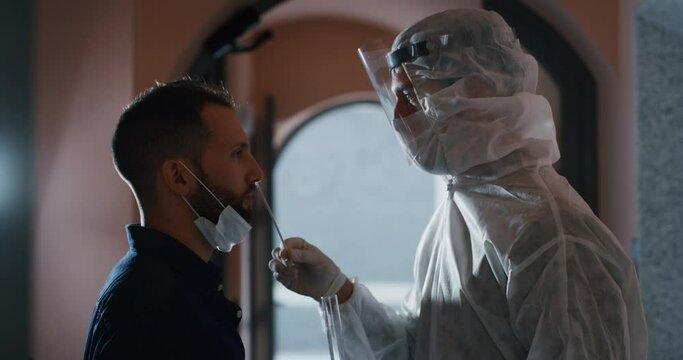 An young man is getting tested at a coronavirus by nasopharyngeal swab by medical staff with PPE suit.