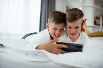 Obraz na płótnie Canvas Two little brothers are playing games on the phone. Beautiful boys enjoying at home..