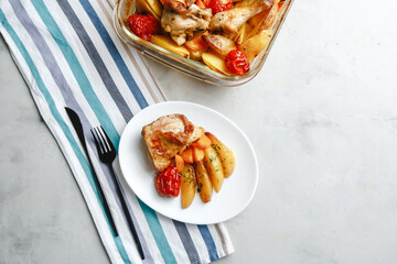 Baked chicken pieces with potatoes, tomatoes, carrots and herbs in a rustic style. Top view, side View on a light background. Close-up and medium plan. Space for text.