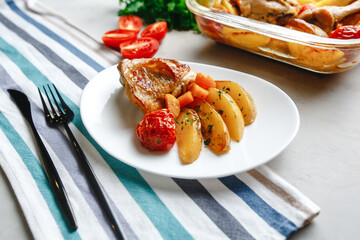 Baked chicken pieces with potatoes, tomatoes, carrots and herbs in a rustic style. Top view, side View on a light background. Close-up and medium plan. Space for text.