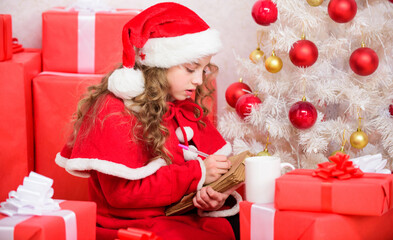 Obraz na płótnie Canvas Wish list. Letter for santa. Kid santa hat enjoy christmas eve. Child writing letter to santa claus. Dear santa. Girl little cute child hold pen and paper near christmas tree. Believe in miracle