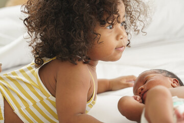 Portrait of first meeting of adorable African little sister and her newborn baby boy on bed at home. New siblings relationship in bedroom at home with love
