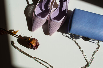 detalle de Zapatos junto a bolso tipo clutch , de color morado y una rosa seca