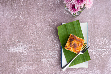 Thai custard cake or Khanom mo kaeng on banana leaf and spoon on white plate with stone background. Egg custard with mung bean flour. Thai dessert famous. Top view with space for text