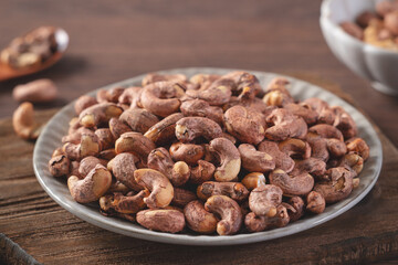 Cashew nuts with peel in a plate on wooden tray.