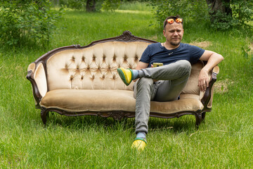 Mid aged man relaxes sitting at comfortable home sofa in garden outdoors. High quality photo.