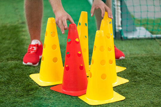 Sports coach preparing training field. Person holding yellow and red training cones on artificial grass field. Coaching sports detail closeup image