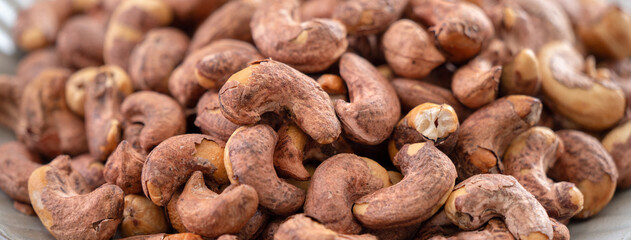 Cashew nuts with peel in a plate on wooden tray.