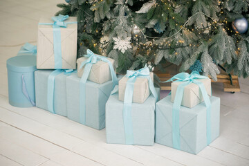 Nice boxes with New Year gifts under Christmas tree on white wooden floor.