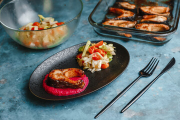 Trout. Baked salmon steaks on a beetroot pillow with vegetable salad, cucumber, tomato, onion, lettuce. Side view, top view.