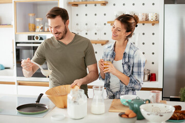 Fototapeta na wymiar Husband and wife making pancakes at home. Loving couple having fun while cooking..