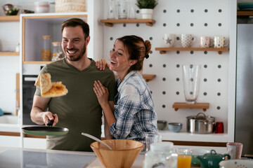 Husband and wife making pancakes at home. Loving couple having fun while cooking..
