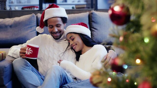 African american man holding cup and laughing with woman near christmas tree