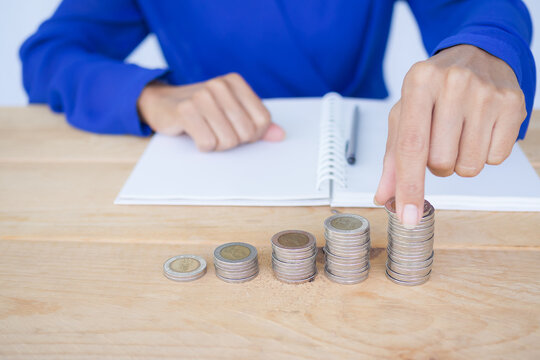 Close up woman holding coin with stack cash and book, pen on wood background. Future finance. saving momey for 2021 year concept.