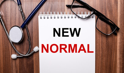 NEW NORMAL is written on white paper on a wooden background near a stethoscope and black-framed glasses. Medical concept