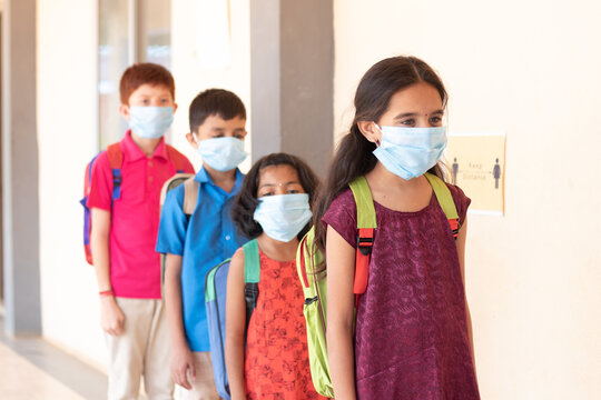 School childrens standing line in front of class while maintaining social distance outside classroom with medical mask wearing - concept of covid-19 or coronavirus safety measures at school.