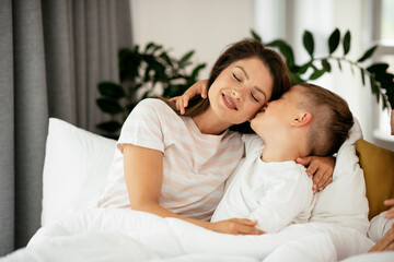Mother and son enjoying in bed. Happy woman with son relaxing in bed.