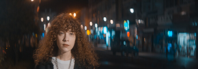 Unhappy attractive woman with curly hair in white t-shirt and black jacket is walking on the street at the night, fashion clothing and feminism concept