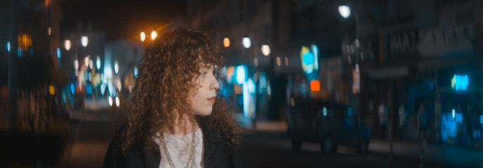Unhappy attractive woman with curly hair in white t-shirt and black jacket is walking on the street...