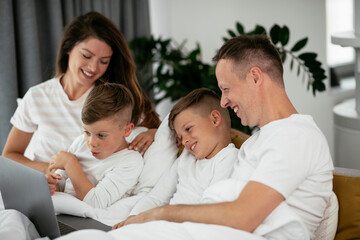 Obraz premium Beautiful parents with kids enjoying at home. Young family watching movie on lap top.
