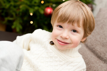 boy in white warm winter sweater with white Teddy bear in Christmas tree background. happy wide smile