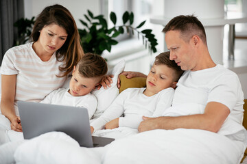 Obraz premium Beautiful parents with kids enjoying at home. Young family watching movie on lap top.