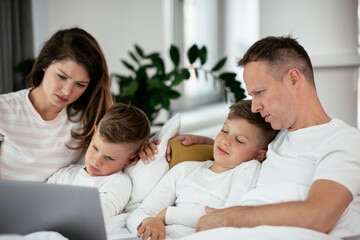 Beautiful parents with kids enjoying at home. Young family watching movie on lap top.