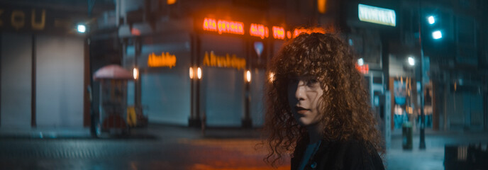 Woman with curly hair in a white shirt and black jacket walks down the red lighting street at the night and turns and looks the back camera - Fashion clothing and feminism concept