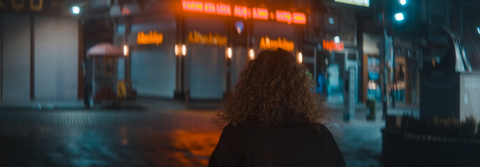 Curly hair woman in a white t-shirt and black jacket leaves a wonderful street with red led lights at the night and she is turns and starts walking, fashion clothing and feminism concept