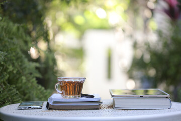 Transparent tea cup with books and phone and tablet on white desk
