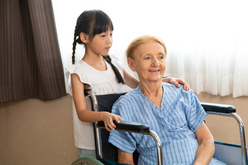 Happy senior patient sitting in wheelchair with grandchild. grandmother and granddaughter enjoying talking together.