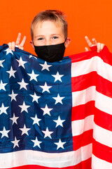 Attractive little boy with the flag of the United States, showing victory on a orange background
