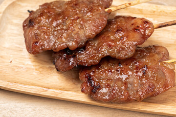 Thai grilled pork in a wooden plate on wooden table.