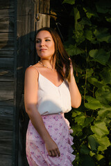 Country girl against the background of a wooden wall and grape leaves, looks thoughtfully somewhere to the side.