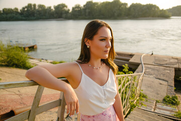 A beautiful girl on the background of the river and the pier, looks into the distance.