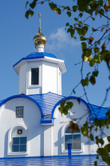 Obraz premium Christian Orthodox Church with christian cross in Russia. White stone walls and blue domes of the Cathedral against a clear sky and green leaves.
