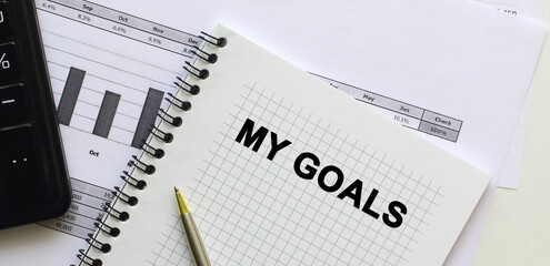 Text on the page of a notepad lying on financial charts on the office desk.