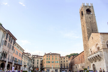 Fototapeta na wymiar Panoramic view of Paolo VI square in Brescia, Lombardy Region - Italy. Sunset scene with clear sky, a stone church tower on the right and bricks houses around the square.
