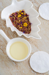 Small white bowls with cosmetic (massage, cleansing) aroma oil, cotton pads, dry herb and flowers. Natural skin care, homemade spa, beauty treatment recipe. 