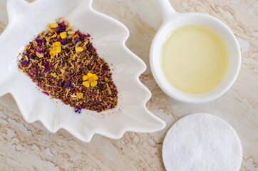 Small white bowls with cosmetic (massage, cleansing) aroma oil, cotton pad, dry herb and flowers. Natural skin care, homemade spa, beauty treatment recipe. Flat lay