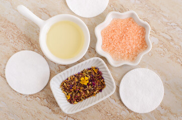 Small white bowls with cosmetic (massage, cleansing) aroma oil, bath salt (foot soak), cotton pads, dry herb and flowers. Natural skin and hair care, homemade spa, beauty treatment.
