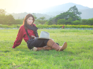 A beautiful western cowgirl sitting on a meadow on a farm after hard work
