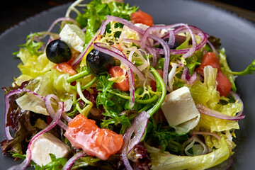 Salad mix with salmon, feta cheese, onions and olives, on a plate, on a wooden background