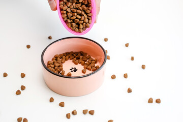Close - up in hand dry cat and dog food is placed in a pink bowl.Pet food on a white background.Healthy and delicious diet for the animal