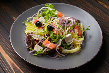 Salad mix with salmon, feta cheese, onions and olives, on a plate, on a wooden background