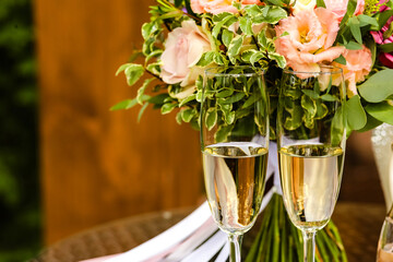 Close-up of two glass glasses of the bride and groom with champagne on the wedding day on the background of a bouquet of pink flowers.Alcoholic drink in a glass.Copy space