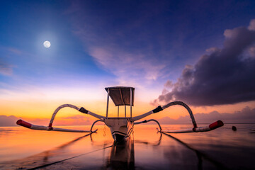 Bali Sanur, traditional fishing boat in sunrise. Close-up in the shallow and calm water with backlight and great sky. jukung