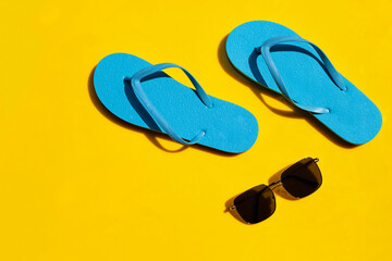 Blue flip flops with sunglasses on yellow background. Enjoy summer holiday concept.